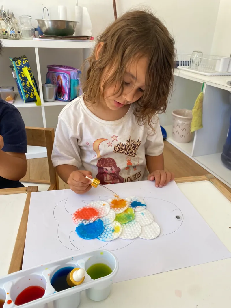 Una niña pinta con colores en una mesa de Aurora.
