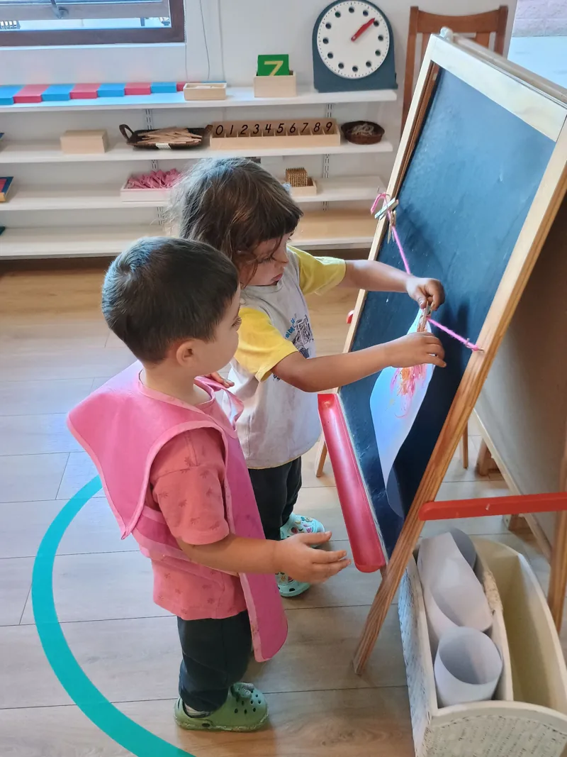 Dos niños pintan en caballetes dentro del ambiente de Aurora.