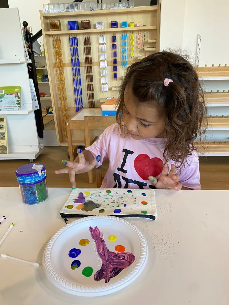 Una niña de Aurora explora colores y pintura con las manos en una mesa de trabajo.